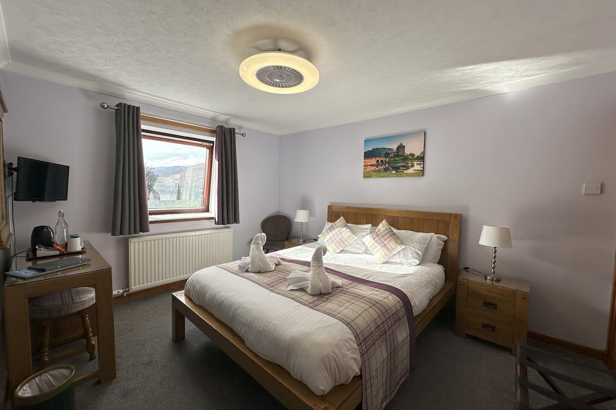 A bedroom with a bed, bedside tables, a desk, a television, and a window with curtains.