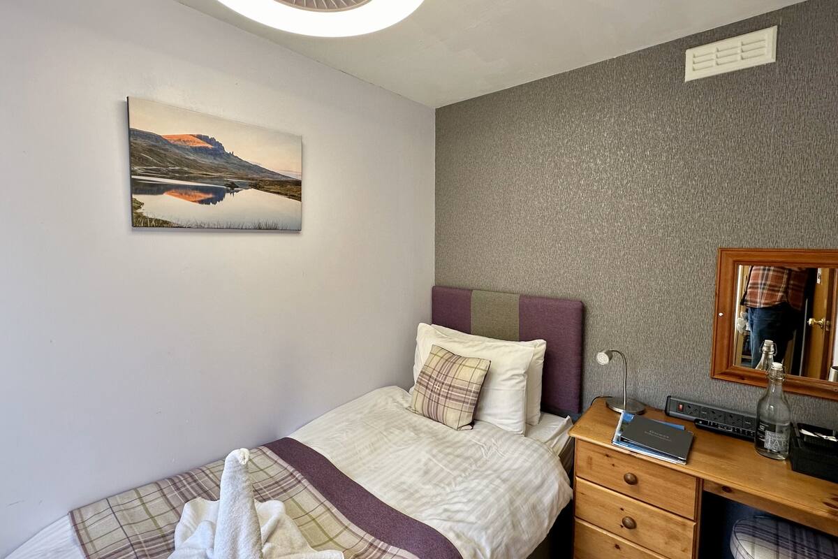 A bedroom with a bed, a bedside table with a lamp, a mirror, and a painting on the wall.
