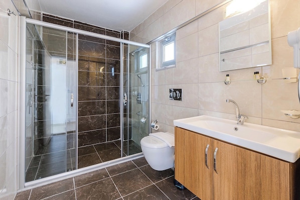 Un baño moderno con ducha de vidrio, inodoro blanco y tocador de madera con lavamanos.