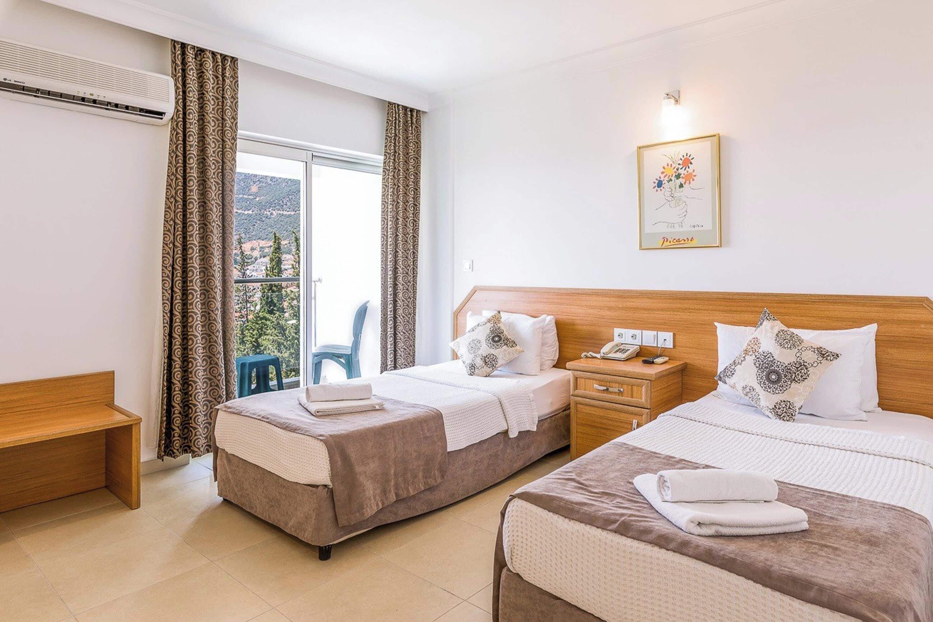 Habitación de hotel con dos camas, cabecera de madera, mesita de noche con teléfono, una obra de arte enmarcada en la pared y vistas al exterior a través de la ventana.