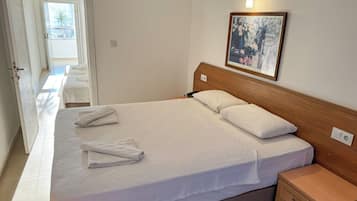 Habitación de hotel con una cama grande, una mesita de noche de madera, un cuadro en la pared y una puerta que da a un balcón.