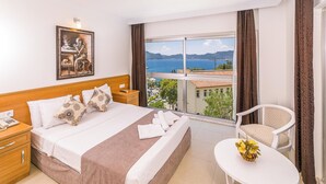 A hotel room with a large bed, a bedside table with a phone, a chair, and a view of the sea and mountains. - Ekici Hotel (Kas)