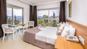 A hotel room with a bed, a chair, a small table, and a phone. The room has large windows with a view of the city and mountains. - Ekici Hotel (Kas)