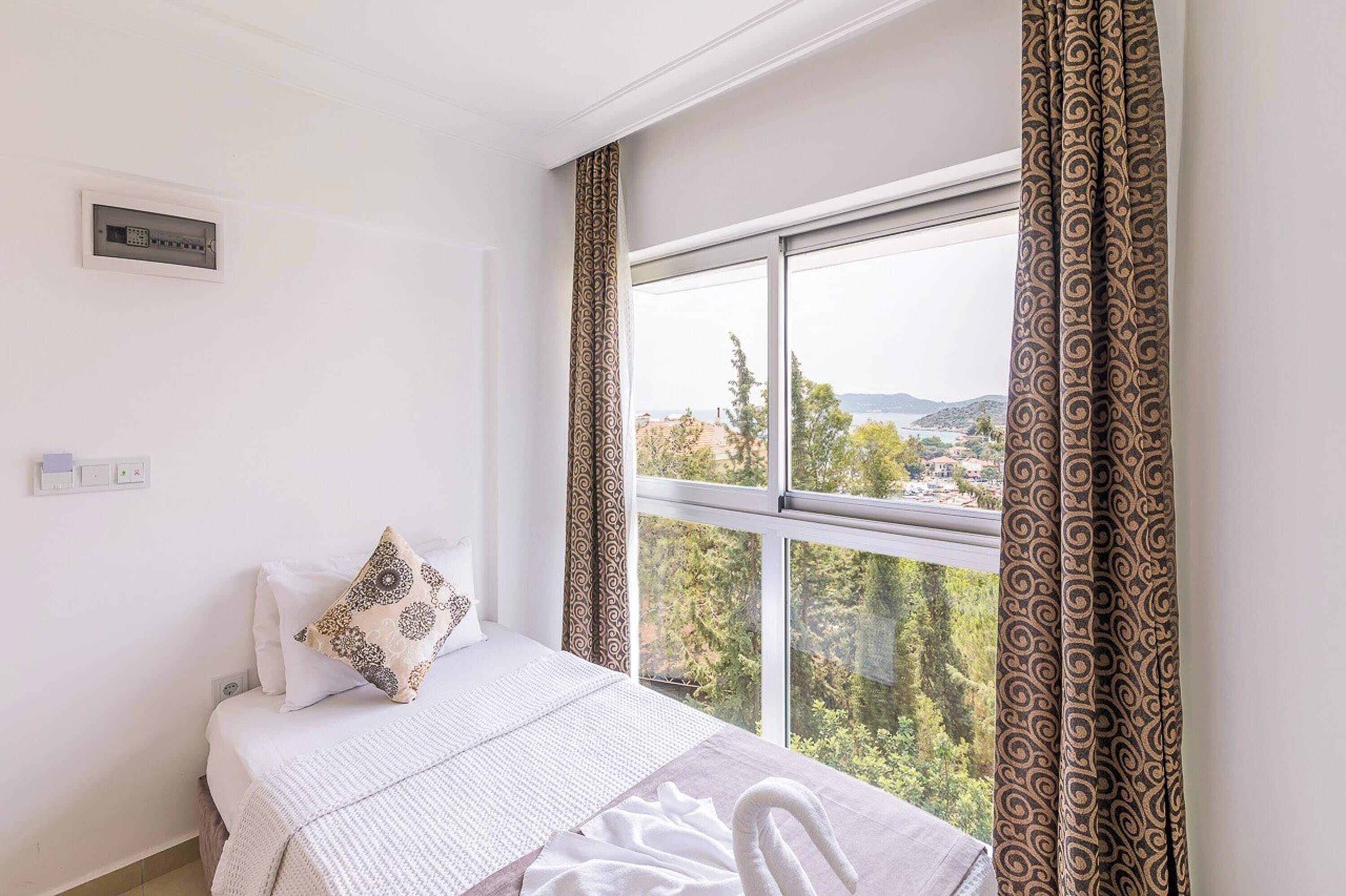 Habitación de hotel con cama, ventana con cortinas, vista al paisaje y un termostato en la pared.