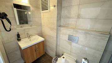 Un baño con lavamanos blanco, armarios de madera, un espejo, inodoro y zona de ducha.