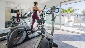 A gym with cardio machines, a large mirror, and a view of the outside. - Hotel Lux isla (Ibiza Town)