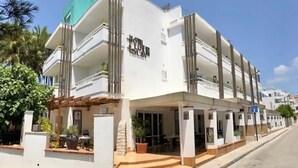 A multi-story hotel with balconies, a covered outdoor seating area, and a clear sky. - Hotel Lux isla (Ibiza Town)