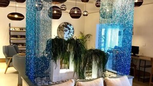 Una sala de estar moderna con una pared decorativa azul, un espejo redondo y una zona de estar con cojines.