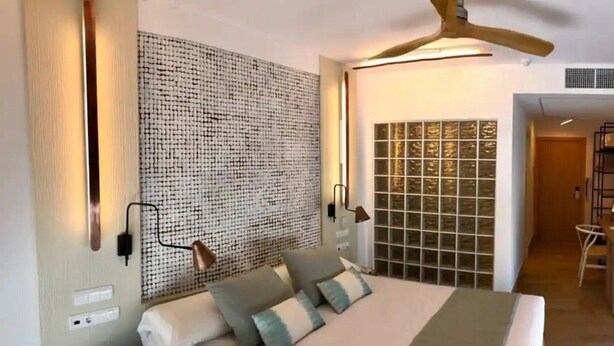 Un dormitorio con una cama, dos lámparas de pared, un ventilador de techo y una pared con textura.