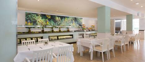 A spacious dining area with white tables and chairs, a large aquarium wall, and a buffet with various food items.