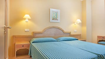A hotel room with a bed, two bedside tables, a nightstand, a wall-mounted lamp, and a framed picture on the wall.