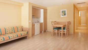 Ett kompakt bostadsutrymme med en soffa, ett matbord, stolar, ett litet kök och en hall.
