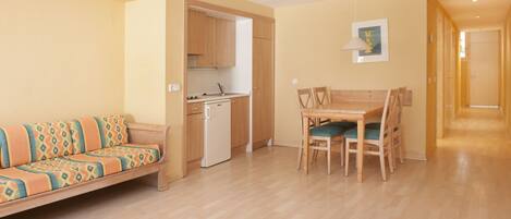 A compact living space with a sofa, dining table, chairs, a kitchenette, and a hallway.