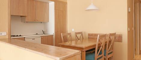 A compact kitchen with wooden cabinets, a dining table with chairs, and a hanging pendant light.