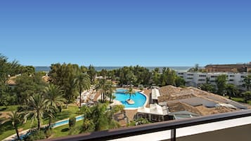 Un resort con una piscina grande rodeada de palmeras y vista al océano.