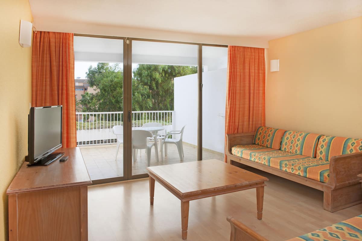 Een kamer met een bank, een televisie, een tafel en een balkon met uitzicht op bomen.