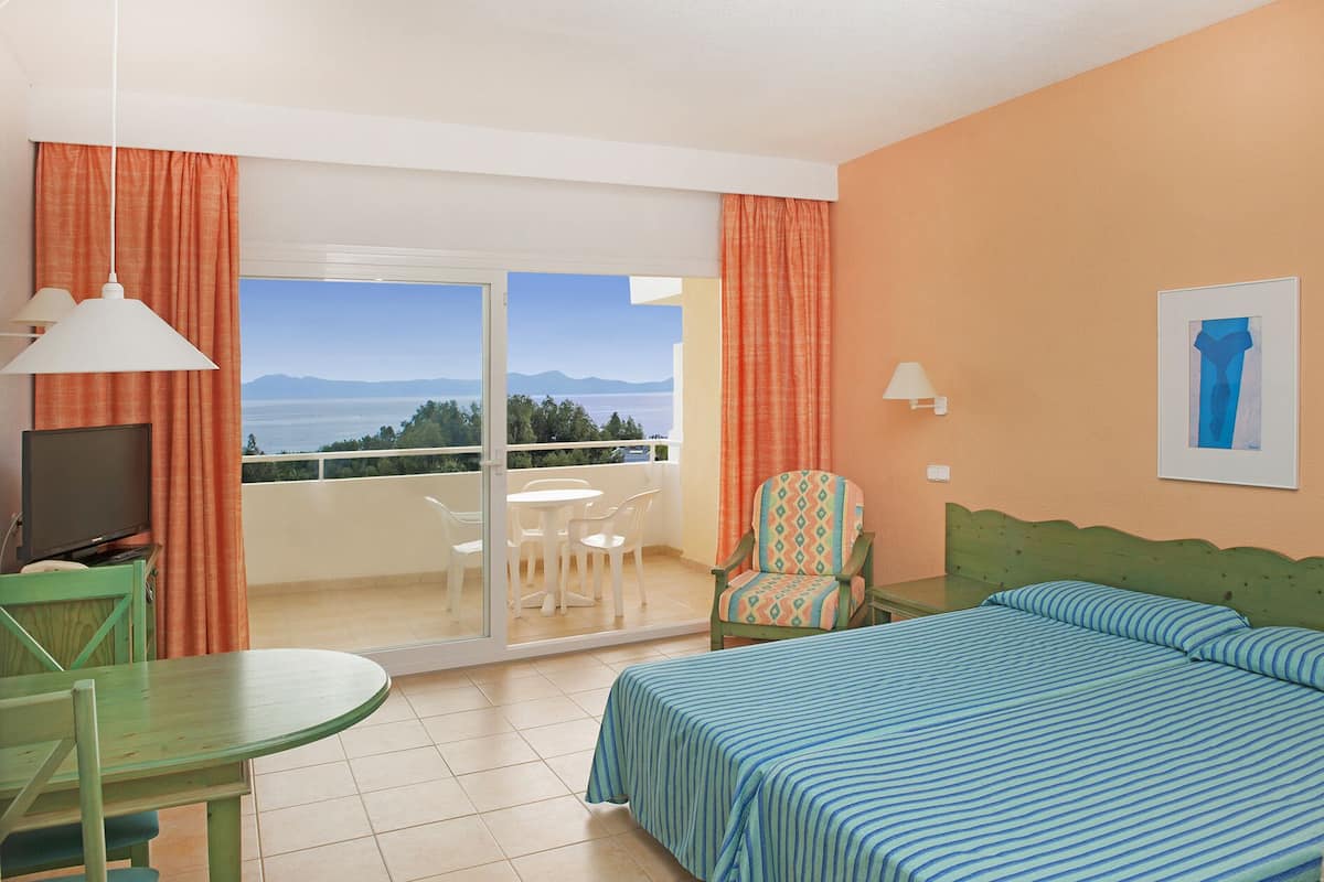 Een hotelkamer met een bed, een stoel, een tafel, een televisie en uitzicht op zee.