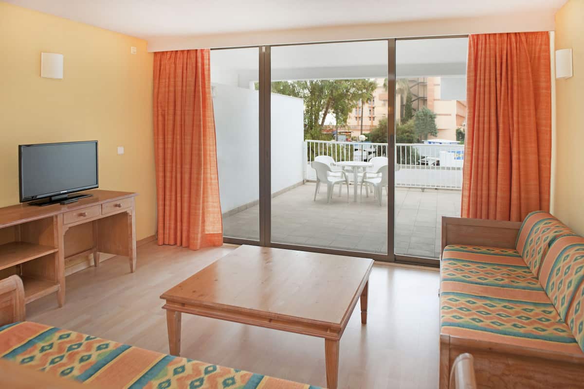 Een kamer met een bank, een televisie op een bureau, een tafel en een balkon met stoelen en een leuning.