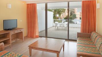 A hotel room with a wooden desk, a television, a sofa, and a balcony with a table and chairs.