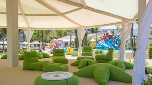 Un espacio al aire libre techado con sillones tipo pufs verdes y una zona de juegos para niños al fondo.