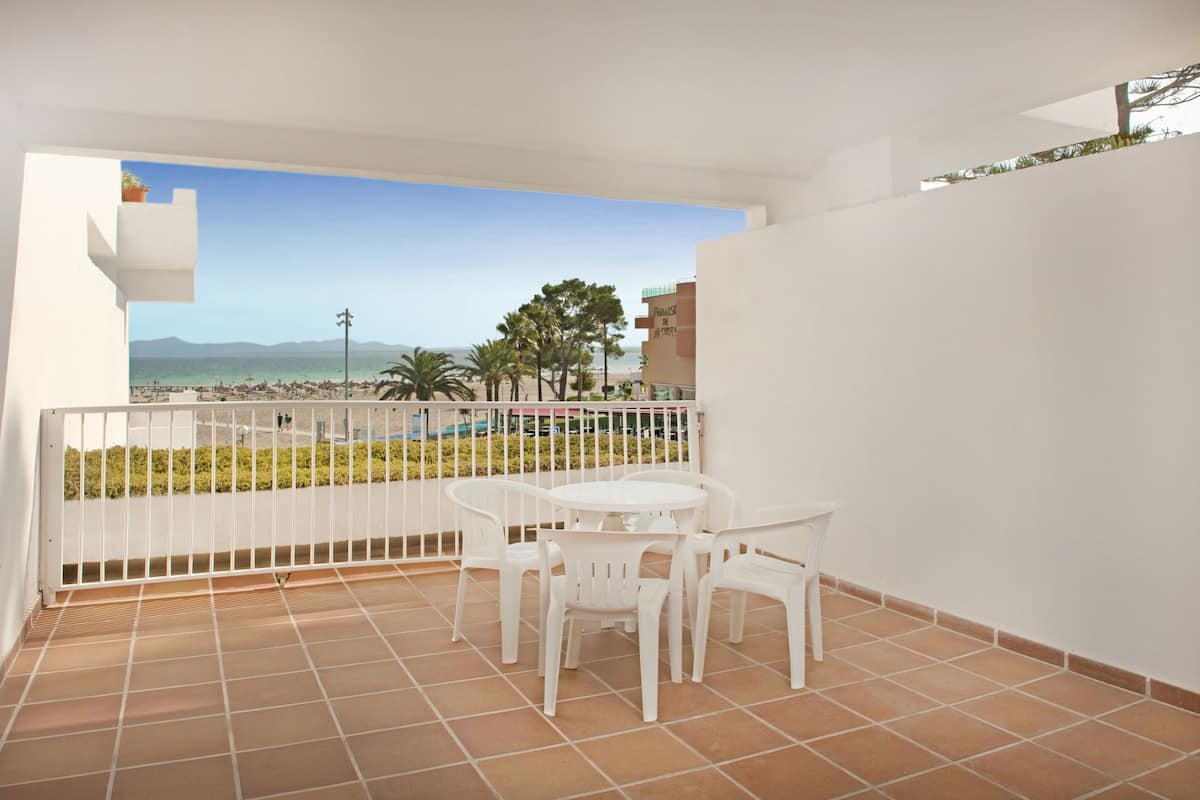 Een balkon met een witte tafel en stoelen, uitzicht op het strand en een betegelde vloer.