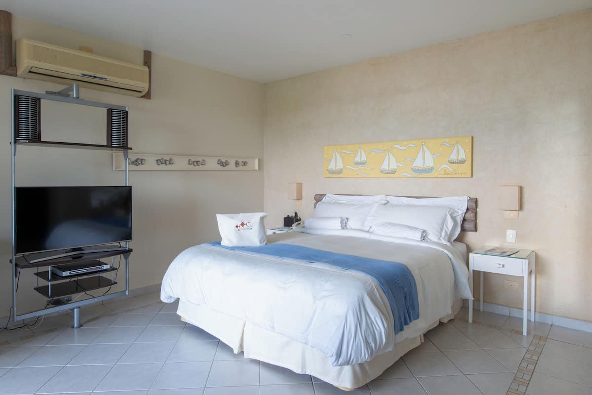 Une chambre d’hôtel avec un lit, un téléviseur, un téléviseur à écran plat posé sur un meuble, un tableau au mur et une petite table avec une lampe.
