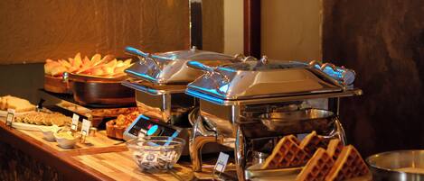 A buffet setup with various food items and a waffle maker.