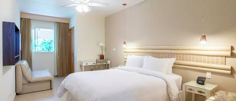Una habitación de hotel con cama, escritorio, silla, ventilador de techo y ventana con cortinas.