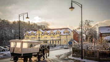 Una escena callejera con un carruaje tirado por caballos, edificios y un paisaje cubierto de nieve.