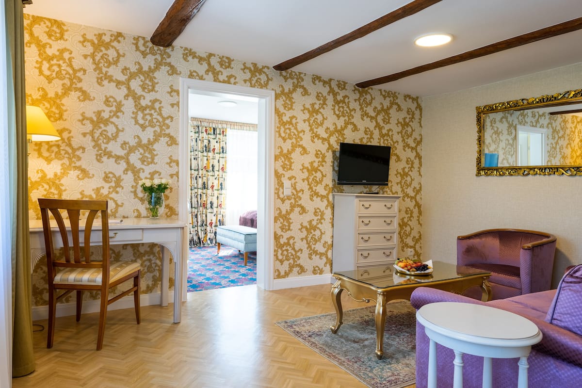 Ein Zimmer mit einem Holztisch, einem Fernseher, einem violetten Sessel und einer gemusterten Tapete.