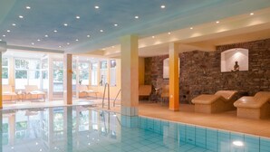 Una piscina interior con baldosas azules brillantes, paredes de piedra y zonas de estar.
