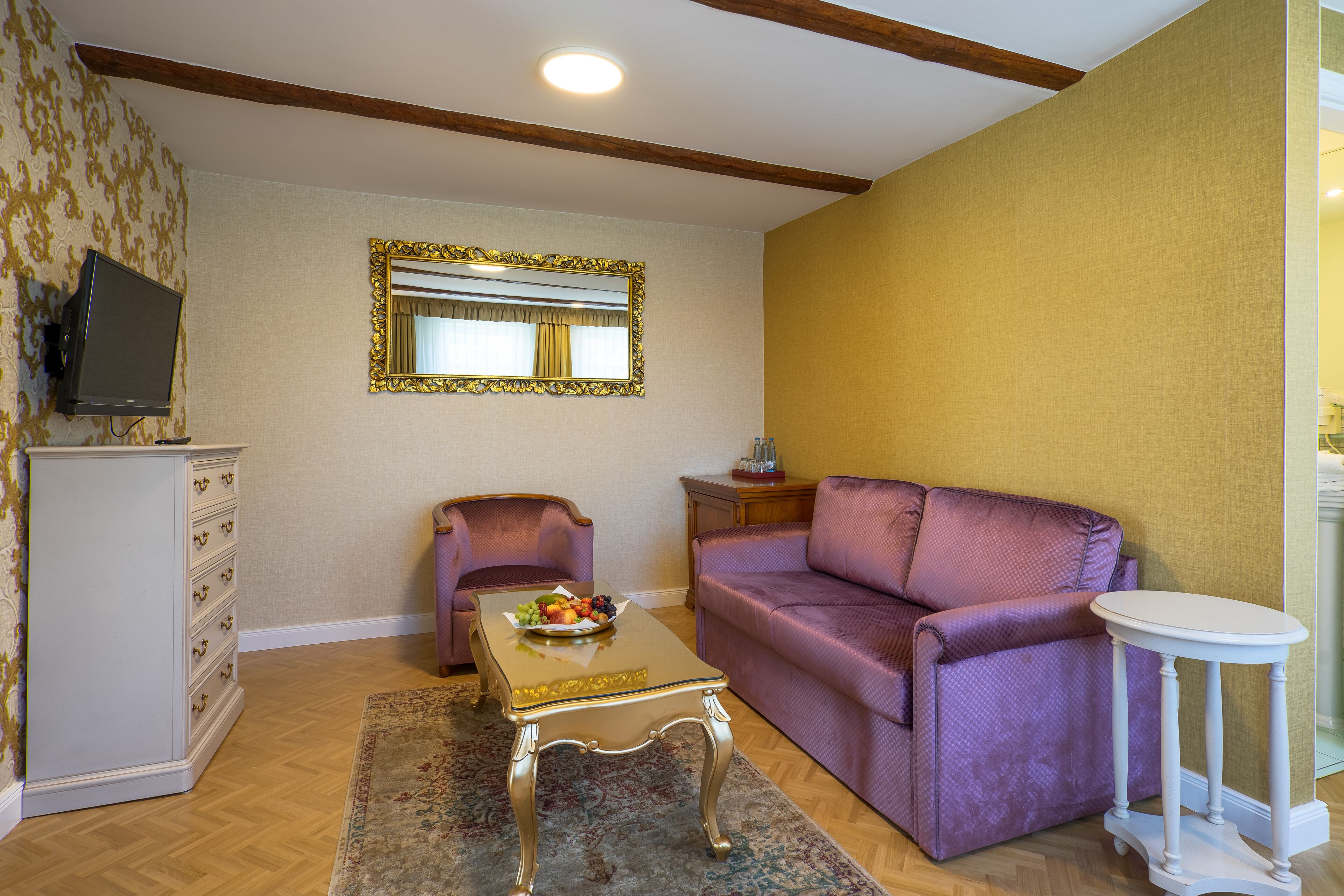 A living room with a purple sofa, a small table with fruit, a television, and a mirror on the wall.