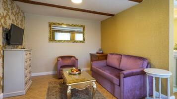 A living room with a purple sofa, a small table with fruit, a television, and a mirror on the wall.