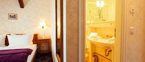 A hotel room with a bed, a nightstand, a lamp, a bathroom with a sink and mirror.