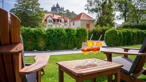 Una mesa de madera con dos vasos de una bebida, un banco y una vista de un castillo al fondo.
