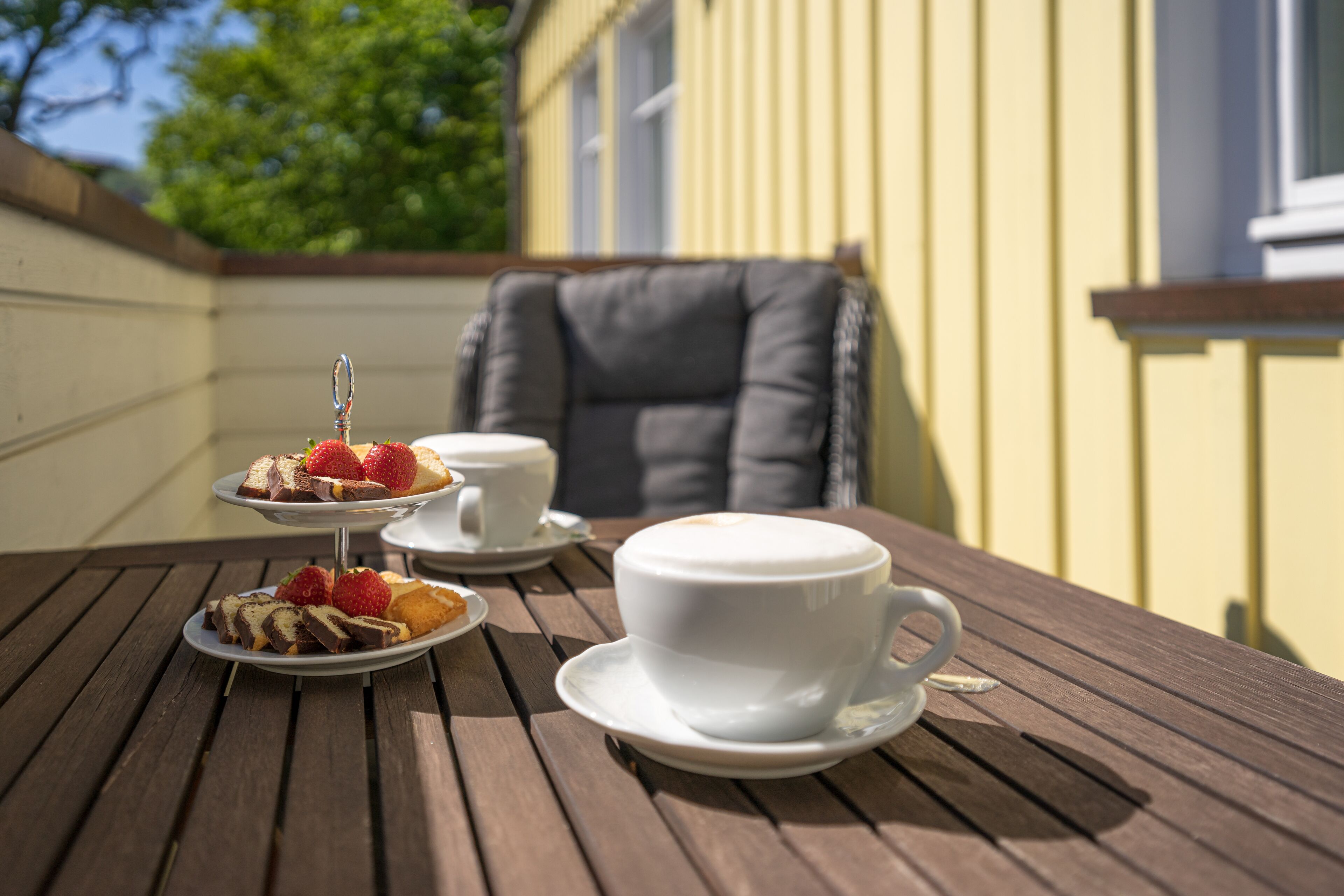 A wooden table with a white cup and saucer, a white teacup, and a dessert tray with strawberries and chocolate.