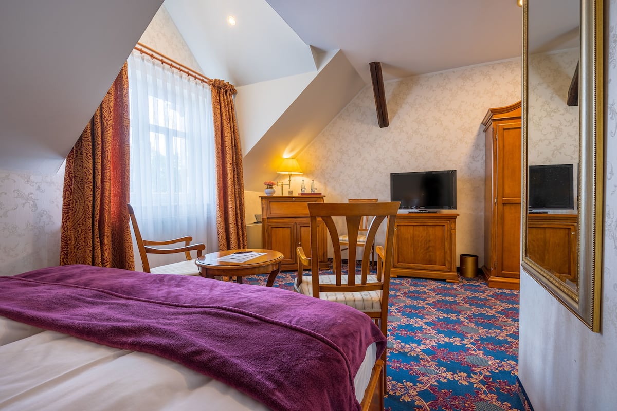 Ein Hotelzimmer mit Bett, Schreibtisch, Stuhl, Fernseher und Spiegel.