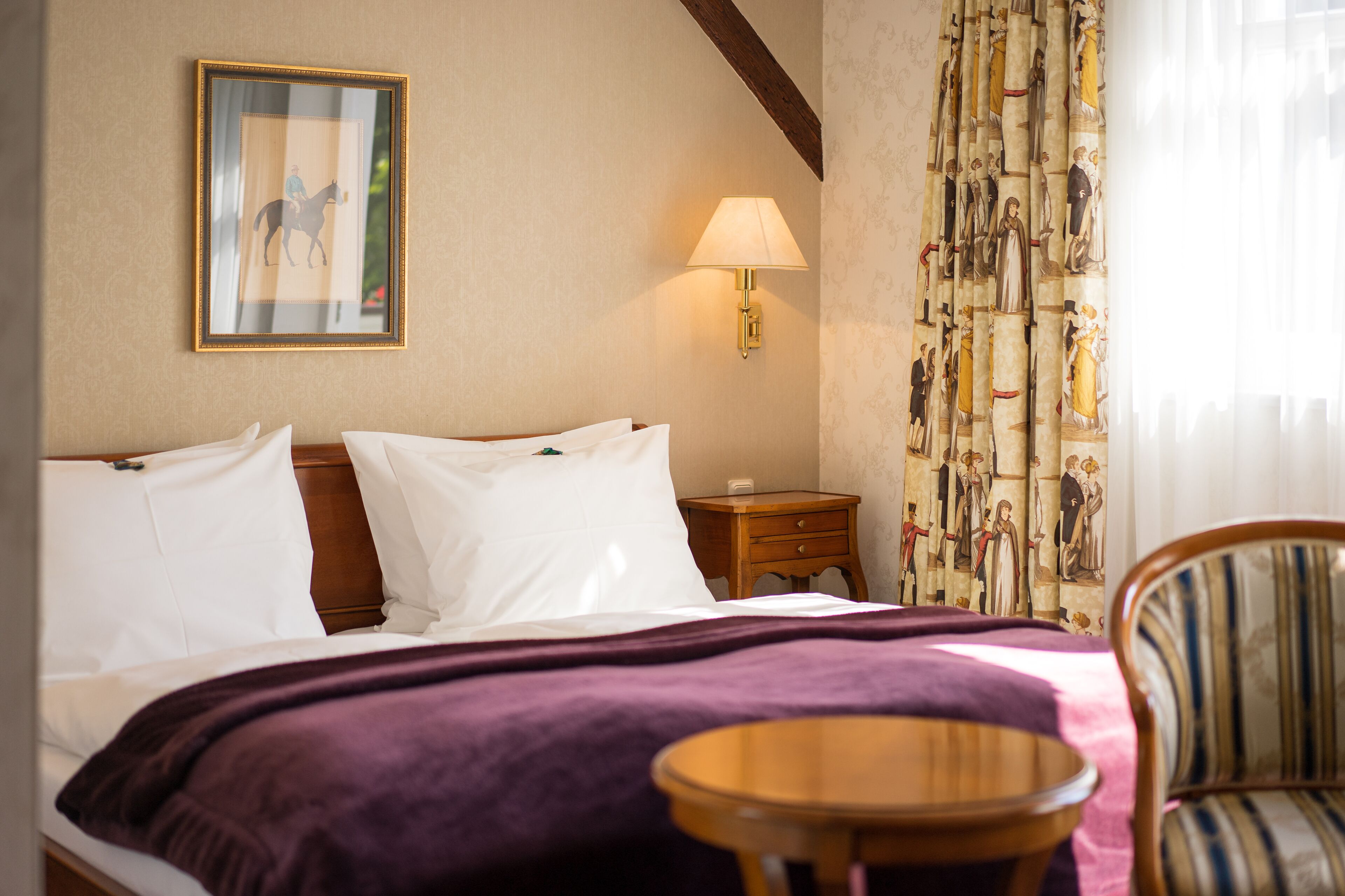 Een hotelkamer met een bed, nachtkastje met een lamp, een stoel en een schilderij aan de muur.