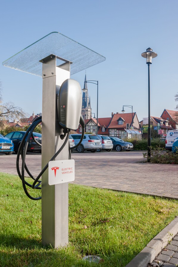 An electric vehicle charging station in a parking lot with houses in the background.