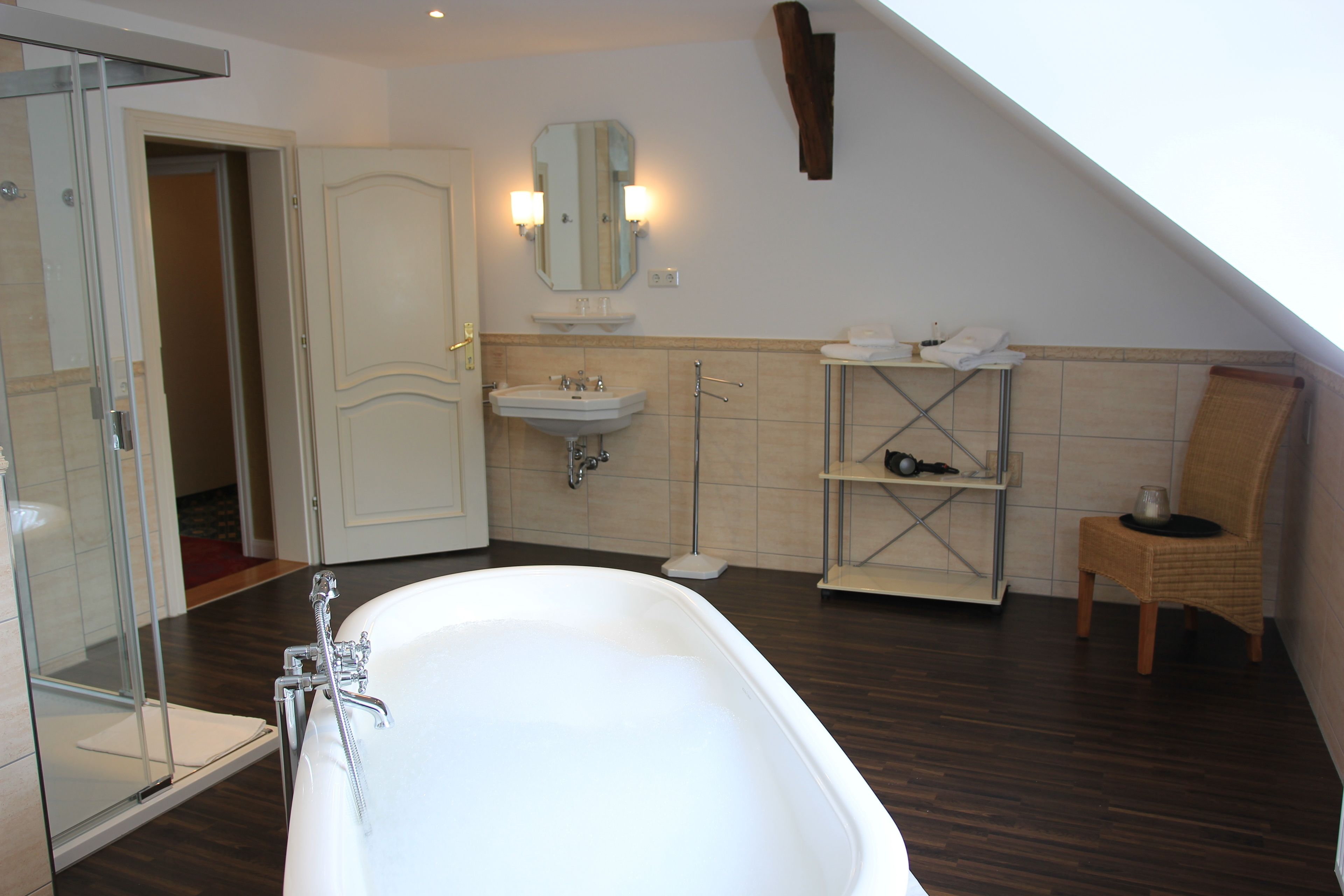 Een moderne badkamer met een vrijstaand bad, een glazen douchecabine, een wastafel met spiegel en een rieten stoel.