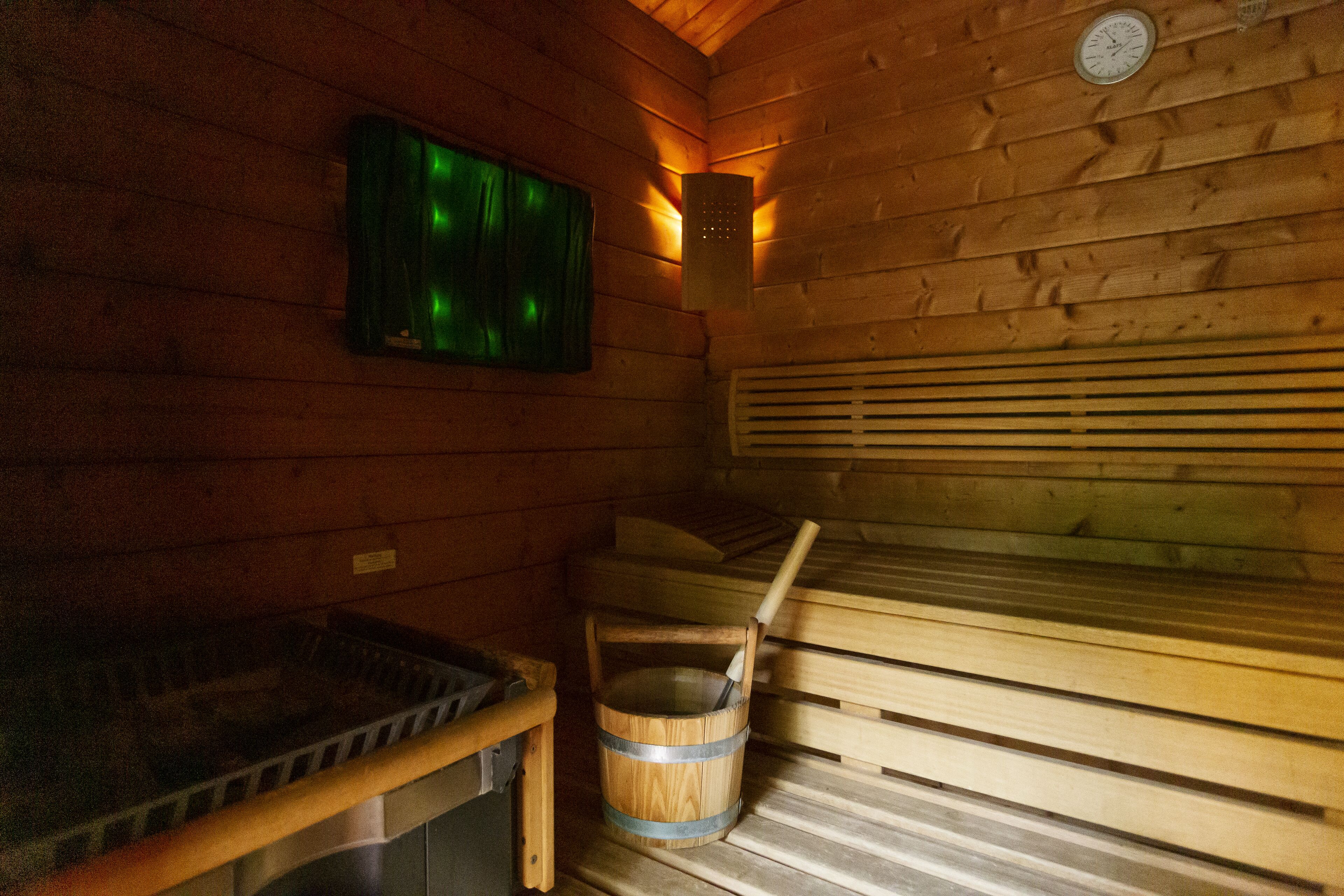 Un cuarto de sauna con bancos de madera, un balde de madera y un calentador fijado a la pared.