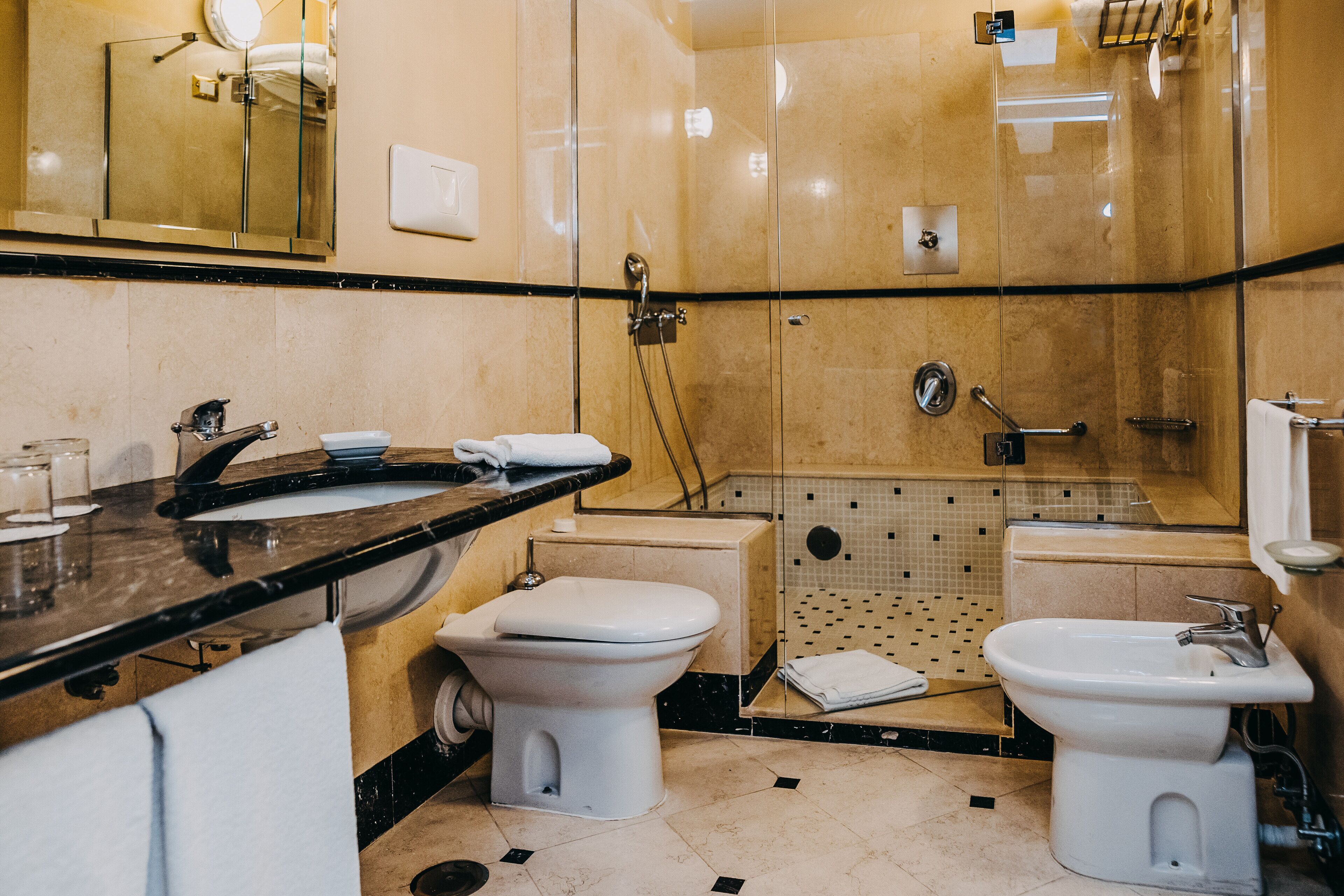 Un bagno moderno con doccia vetrata, due lavandini e un water.
