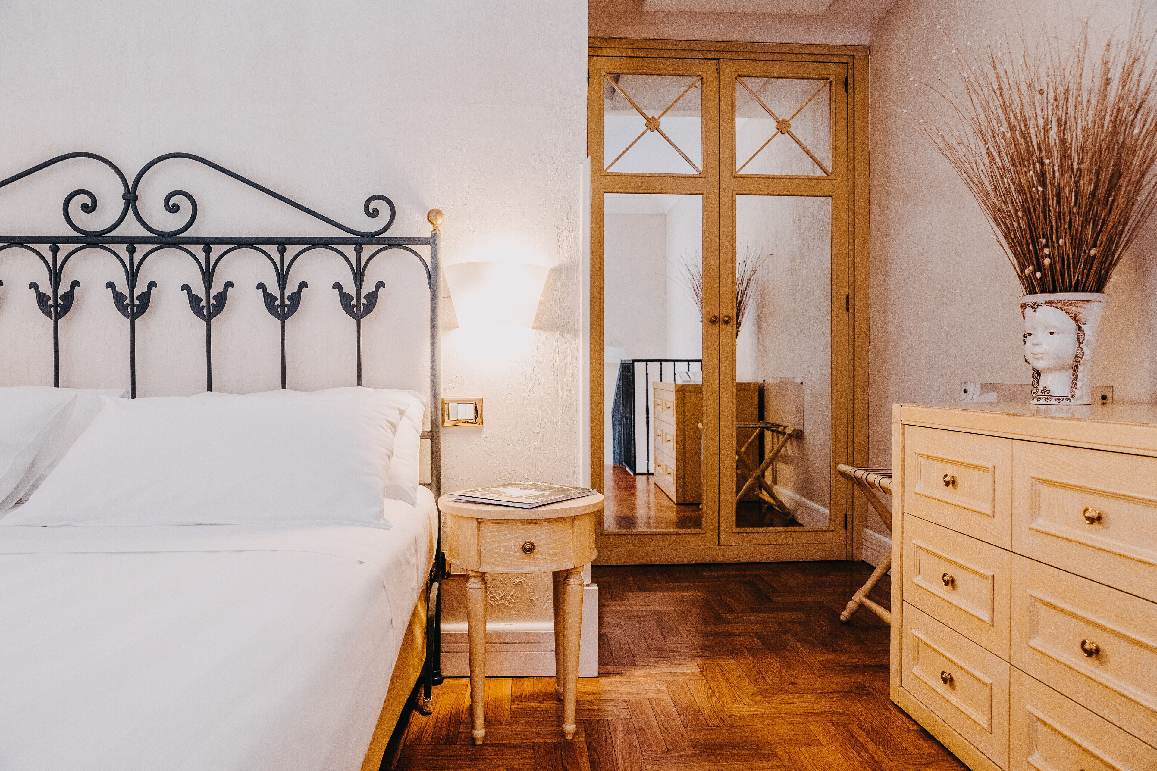 A bedroom with a bed, bedside table, lamp, dresser, and a mirror.
