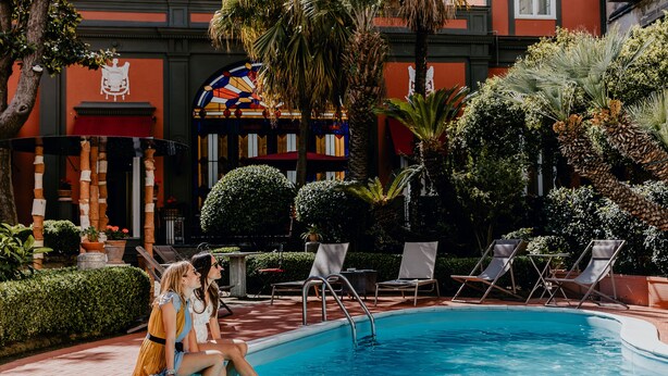 A pool area with lounge chairs and a building with a colorful stained glass window. - Costantinopoli 104 (Naples)
