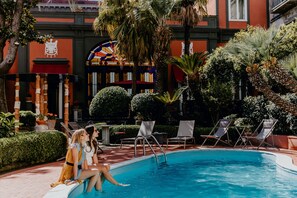 A pool area with lounge chairs and a building with a colorful stained glass window. - Costantinopoli 104 (Naples)