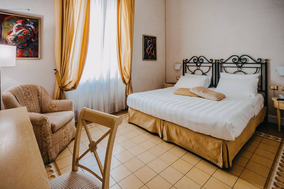 A hotel room with a bed, a chair, a desk, and a window with curtains.
