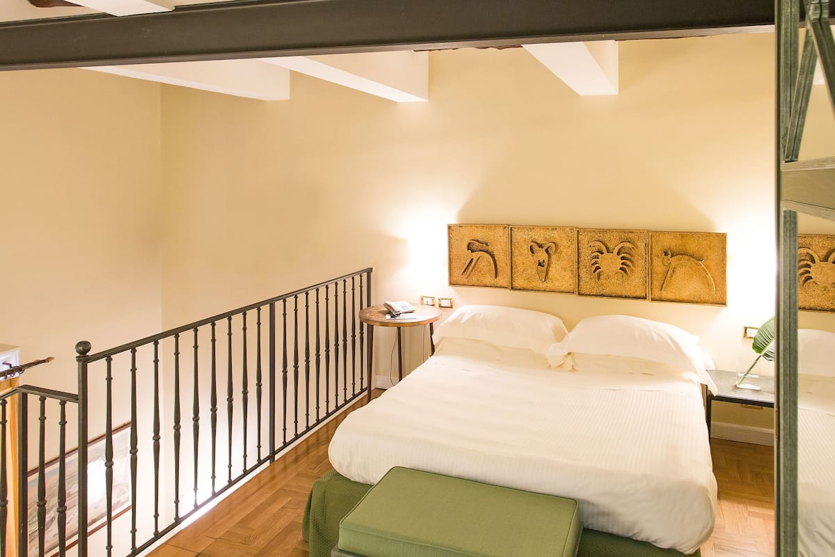 A bedroom with a wooden ceiling, a bed with green bedding, a bench, and a railing along the balcony.