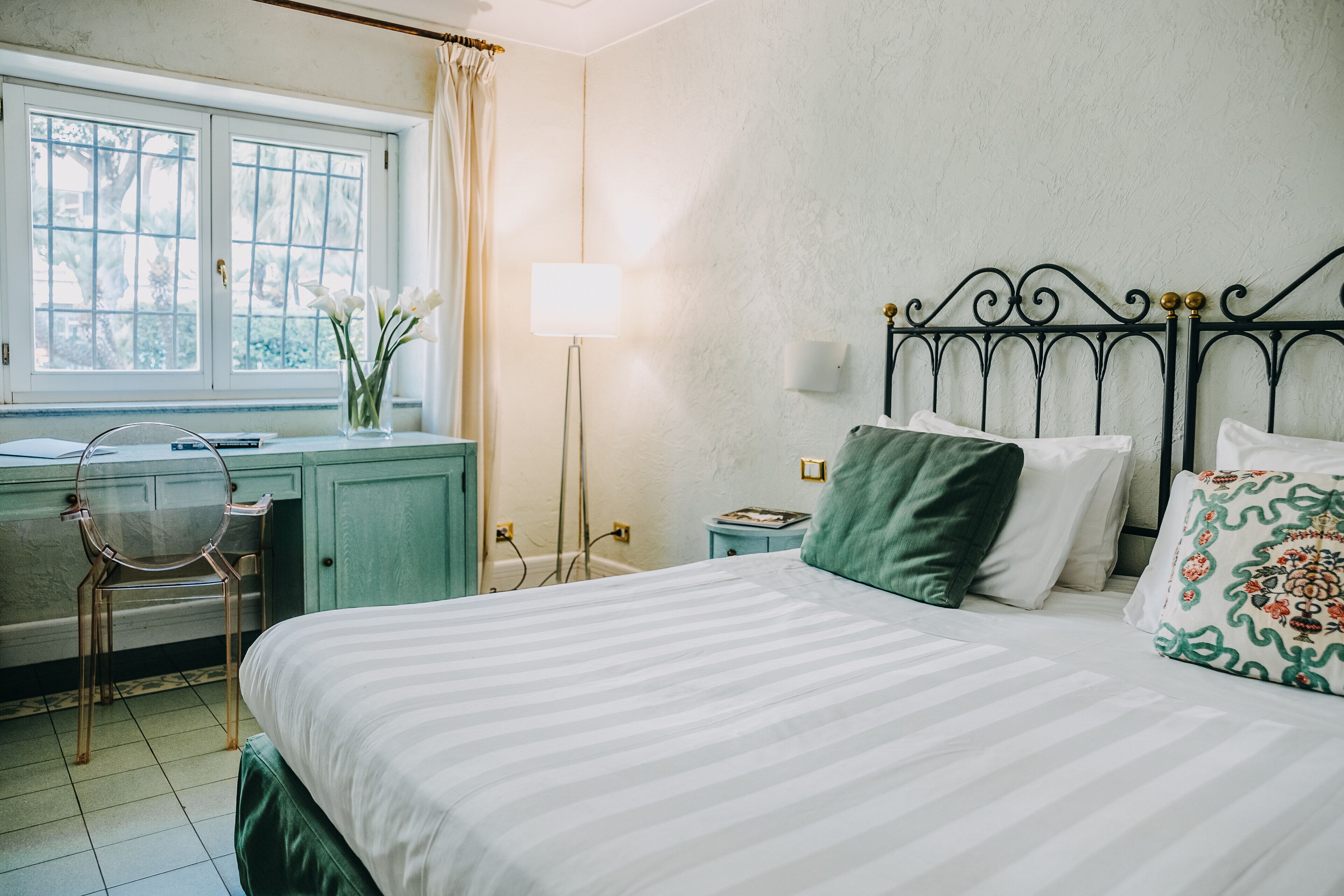 Une chambre à coucher avec un lit, un bureau, une chaise, une lampe et une fenêtre avec des rideaux.