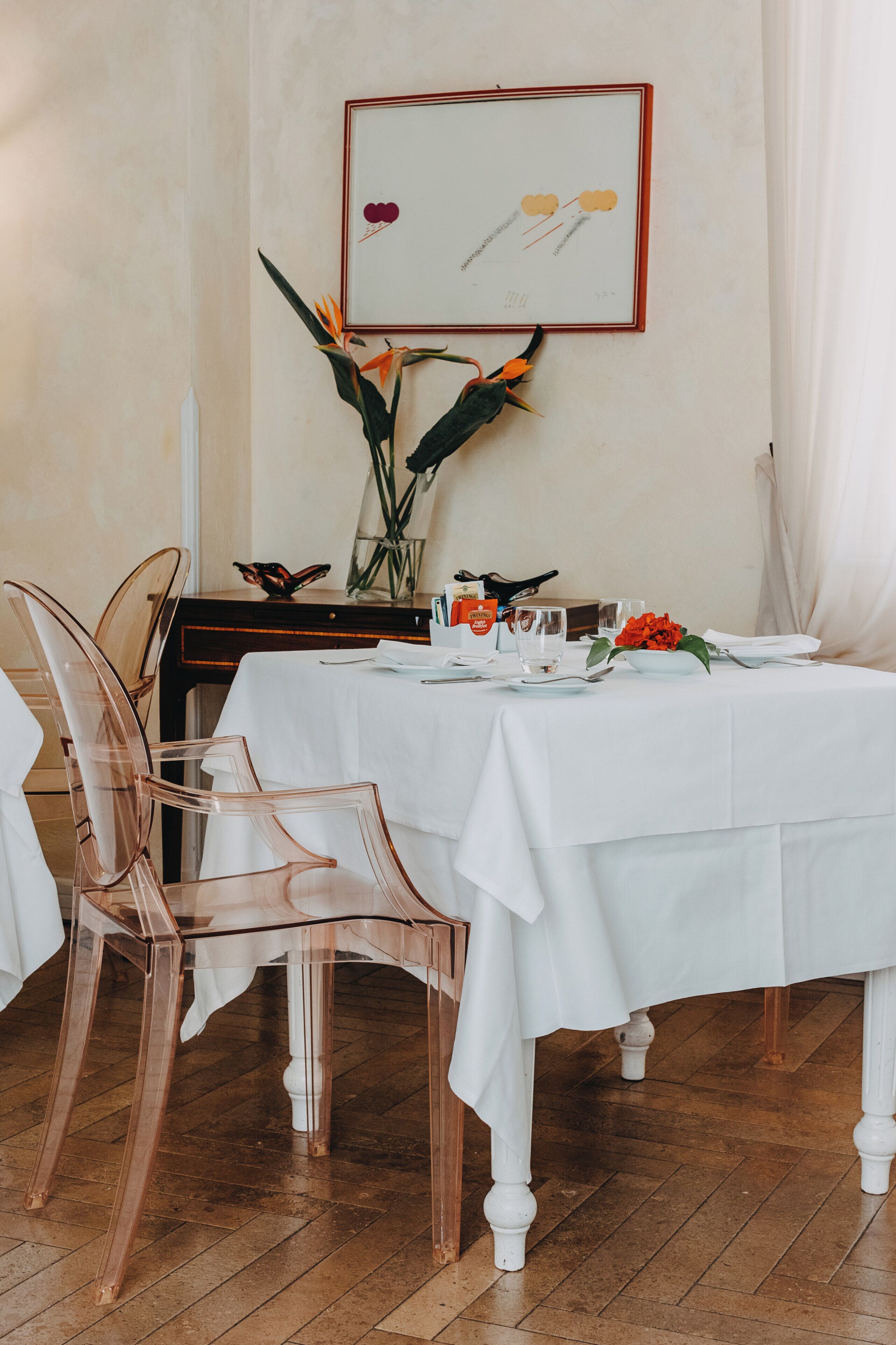 Un tavolo da pranzo apparecchiato con sedie trasparenti, un vaso con fiori e un quadro appeso al muro.
