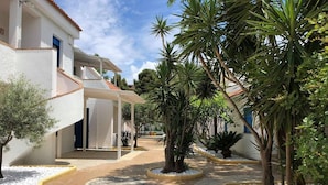 Un patio con un camino empedrado, palmeras y un edificio de fachada blanca y techo de tejas rojas.